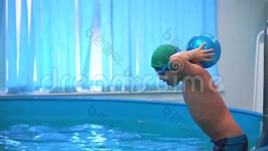 一个带<strong>泳镜</strong>的男孩在游<strong>泳</strong>池里扔一个蓝色的球，跳进水里。